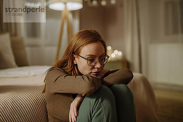 Traurige Frau mit Brille sitzt zu Hause vor dem Bett