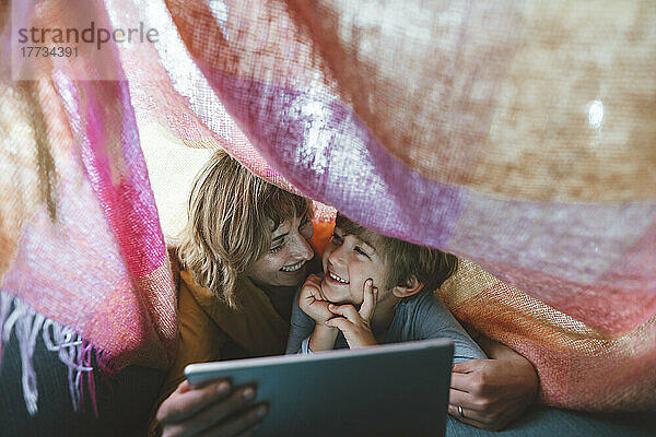 Fröhliche Mutter und Sohn mit Tablet-PC unter Decke liegend