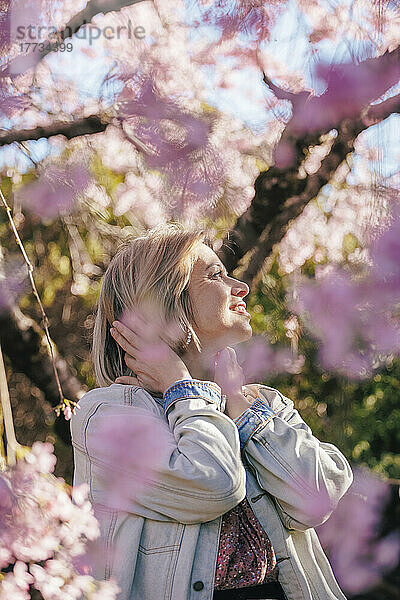 Lächelnde blonde Frau steht an einem sonnigen Tag im Garten