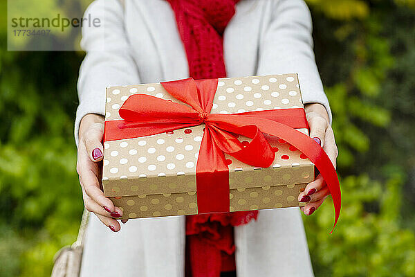 Junge Frau überreicht Weihnachtsgeschenk mit roter Schleife