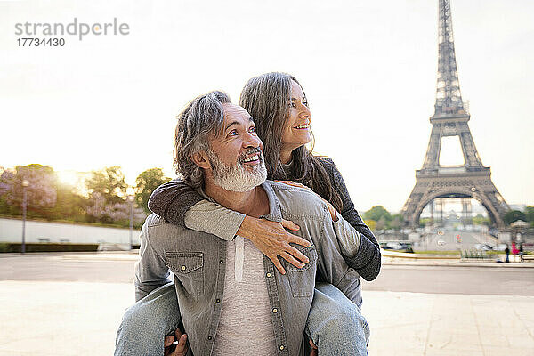 Lächelnder reifer Mann  der einer Frau Huckepackfahrt vor dem Eiffelturm  Paris  Frankreich  gibt