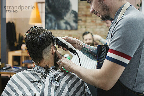 Friseur schneidet Mann mit Elektrorasierer im Friseursalon die Haare