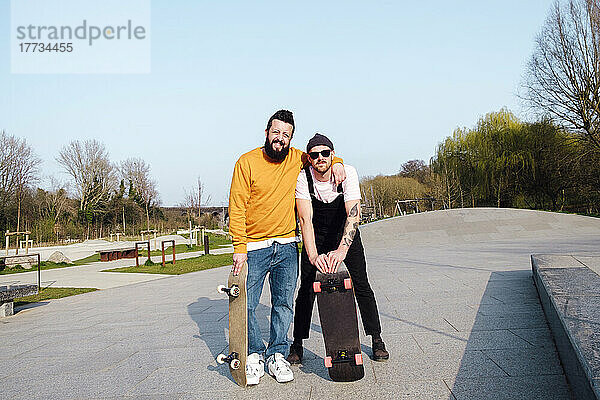 Freunde stehen an einem sonnigen Tag mit Skateboard im Skatepark