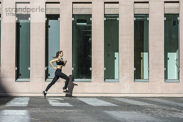 Junge Frau joggt auf Fußweg am Gebäude