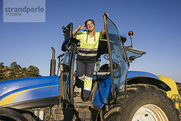 Glückliche Bäuerin gestikuliert Friedenszeichen im Traktor