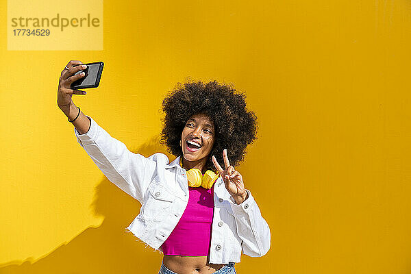 Glückliche Frau macht ein Selfie mit dem Handy vor einer gelben Wand