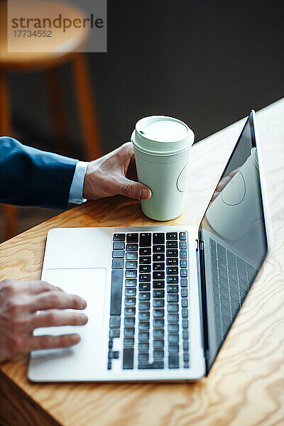 Hände eines Freiberuflers mit Kaffeetasse und Laptop im Café