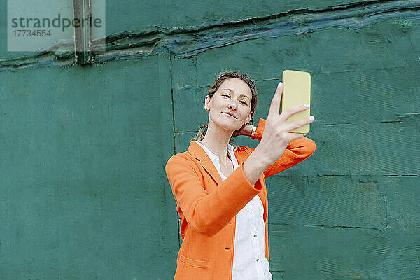 Schöne Frau  die ein Selfie mit ihrem Smartphone an einer grünen Wand macht