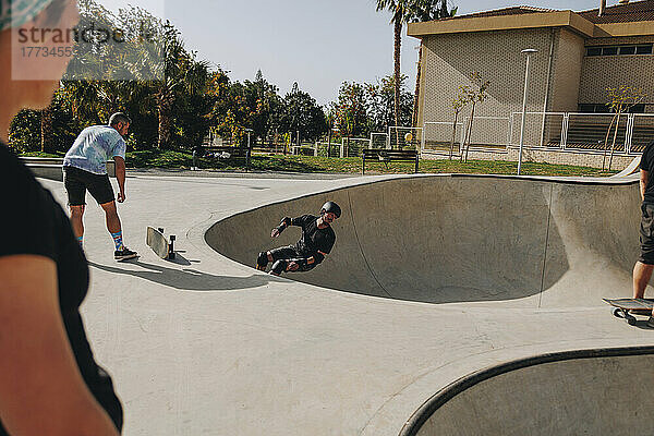 Mann fährt Skateboard auf Sportrampe inmitten von Freunden im Park