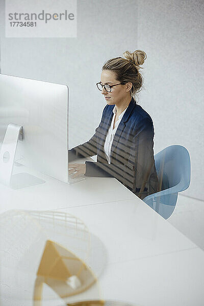 Geschäftsfrau benutzt Desktop-PC am Schreibtisch  gesehen durch Glas