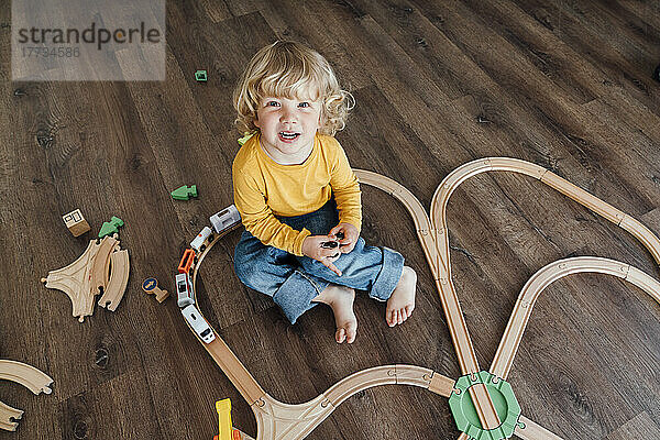 Fröhlicher Junge mit blonden Haaren  der zu Hause mit einer Spielzeugeisenbahn spielt