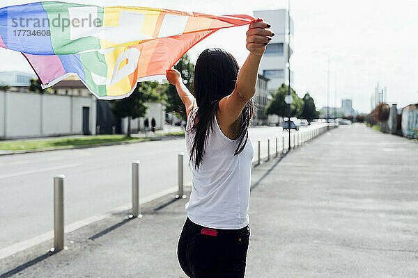 Junge Frau steht an einem sonnigen Tag mit Regenbogenfahne