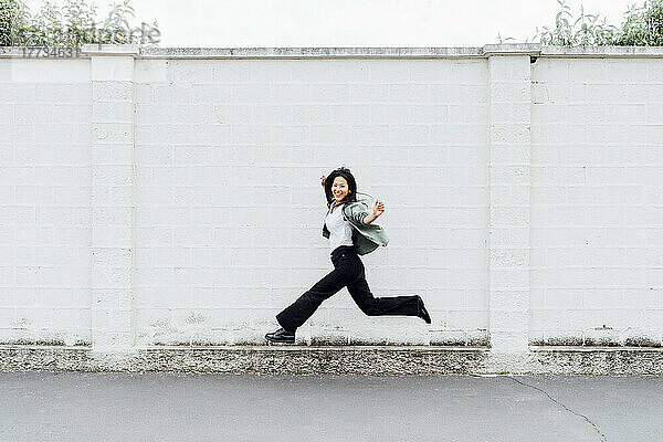 Happy woman jumping in front of wall