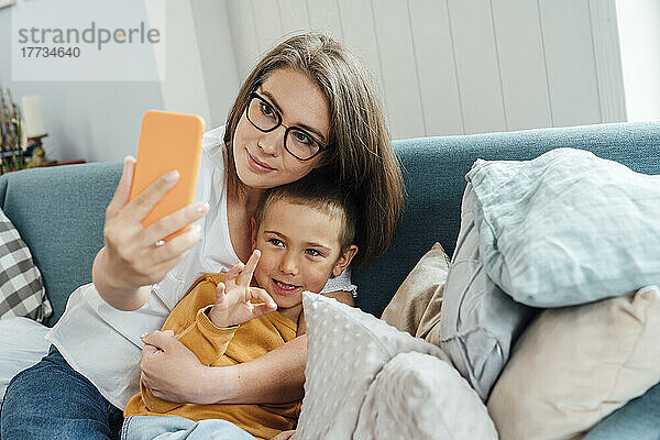 Lächelnde Frau mit Sohn  die zu Hause ein Selfie per Smartphone macht