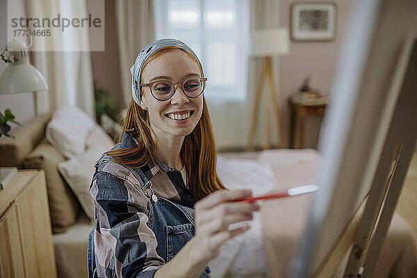 Glückliche Frau mit Brille und Kopftuch übt zu Hause Malen