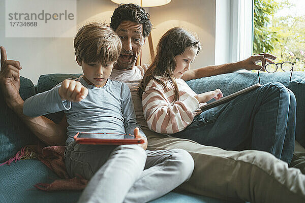 Glücklicher Vater sitzt mit Tochter und Sohn zu Hause am Tablet-PC