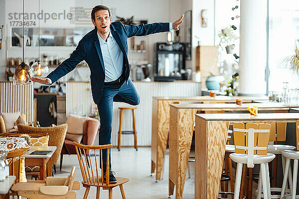 Geschäftsmann mit ausgestreckten Armen steht auf einem Stuhl im Café