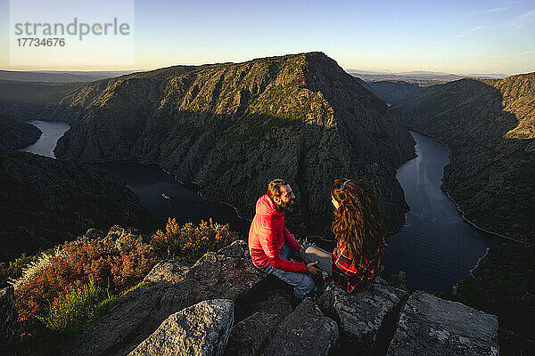Junges Paar sitzt auf dem Gipfel eines Berges am Fluss Sil