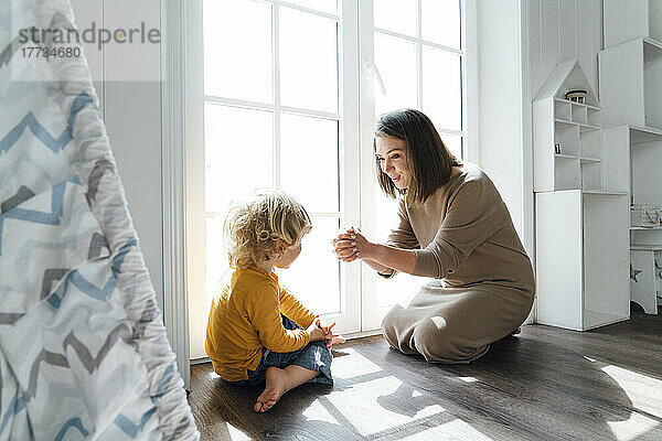 Glückliche Mutter spielt mit ihrem Sohn  der zu Hause am Fenster sitzt