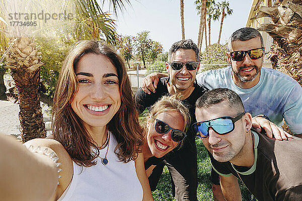 Lächelnde junge Frau  die an einem sonnigen Tag ein Selfie mit Freunden macht