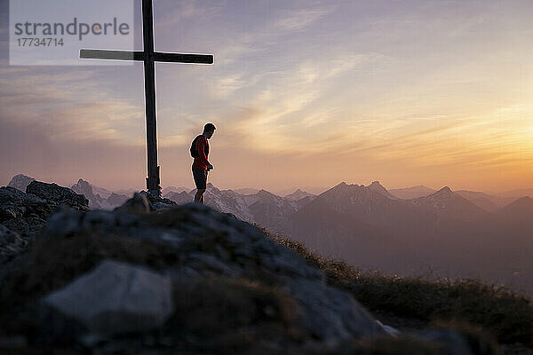 Wanderer steht am Gipfelkreuz am Berg