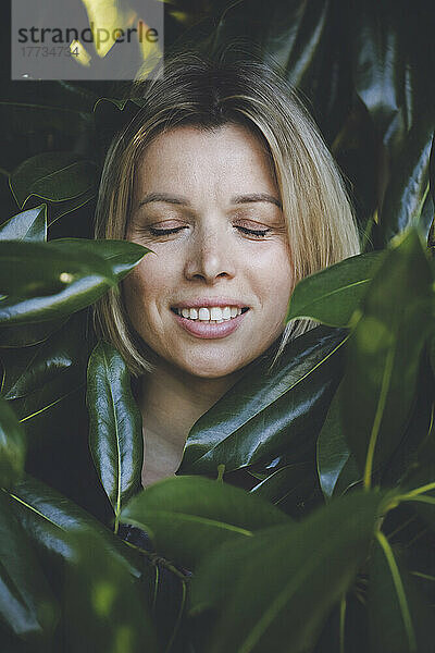 Woman with eyes closed amidst green leaves