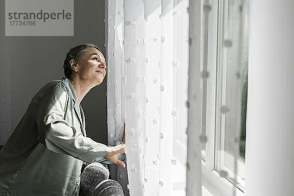 Reife Frau zu Hause  die aus dem Fenster schaut