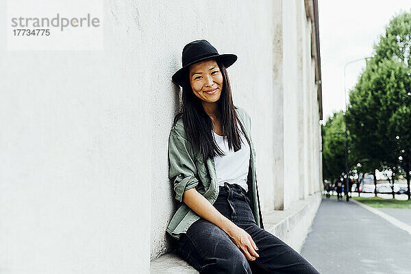 Beautiful smiling woman wearing hat sitting on wall