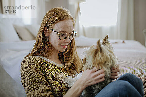 Frau mit Brille sitzt mit Hund zu Hause am Bett