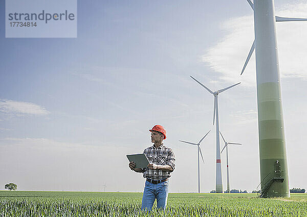 Ingenieur mit digitalem Tablet steht an sonnigem Tag in der Nähe einer Windkraftanlage