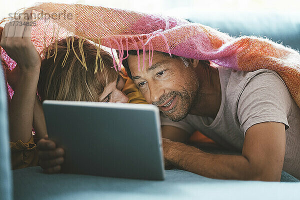 Reifer Mann und Frau mit Tablet-PC unter Decke liegend