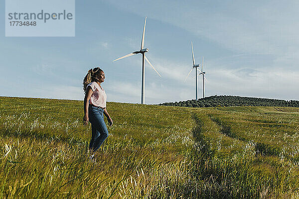 Lächelnde junge Frau  die auf der Wiese vor einer Windkraftanlage läuft