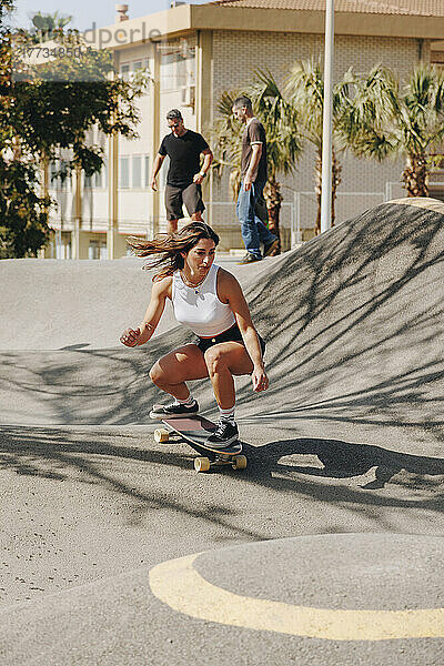 Junge Frau fährt Skateboard auf der Sportrampe mit Freunden im Hintergrund