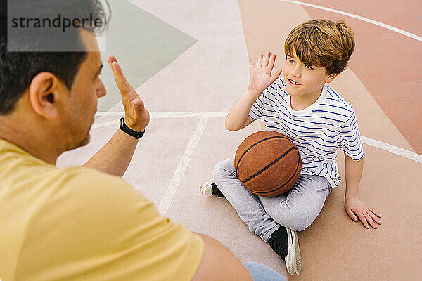 Junge mit Basketball gibt seinem Vater auf dem Sportplatz High Five
