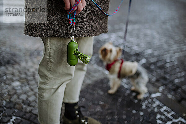 Frau mit Kotbeutelspender steht neben Hund auf Straße