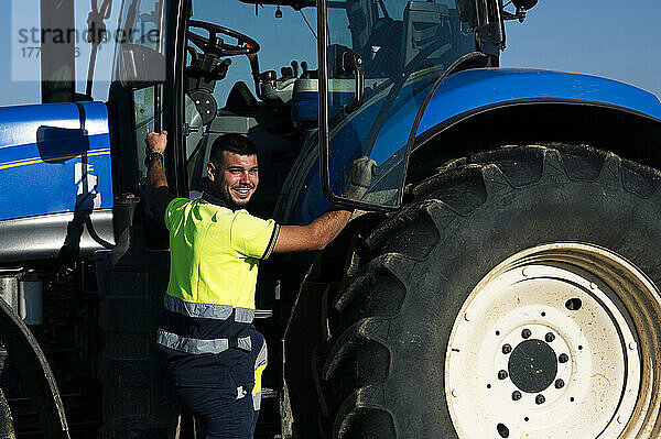 Smiling farmer standing by tractor on sunny day