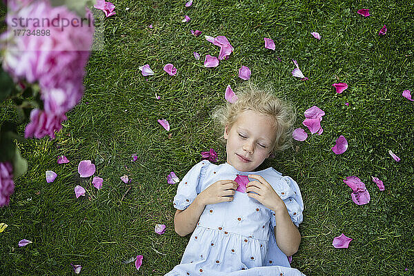 Mädchen mit geschlossenen Augen hält ein Rosenblatt in der Hand und ruht im Gras