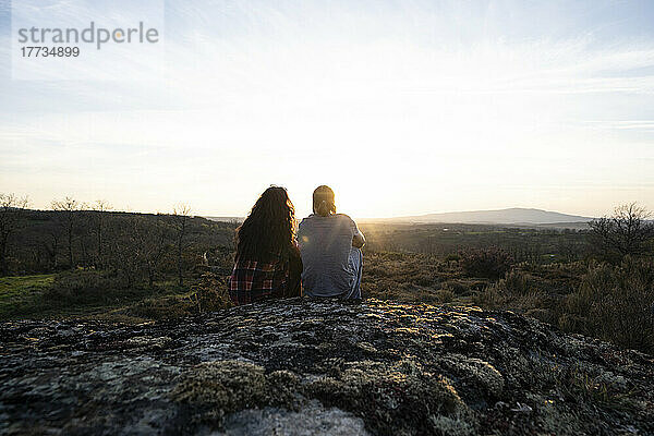 Junges Paar sitzt auf Felsen und bewundert den Sonnenuntergang
