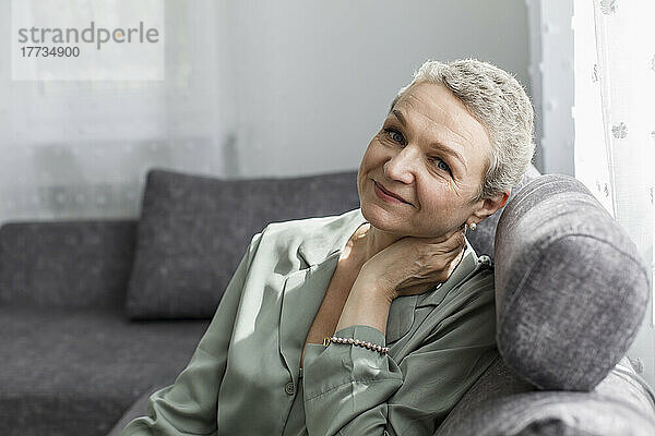 Porträt einer selbstbewussten reifen Frau  die auf der Couch im Wohnzimmer sitzt