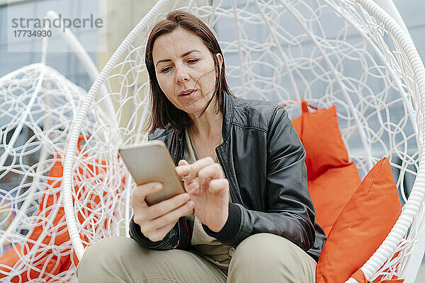 Frau sitzt auf Hängesessel und benutzt Smartphone
