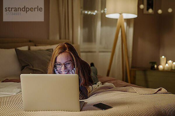 Happy woman with laptop lying on bed at home