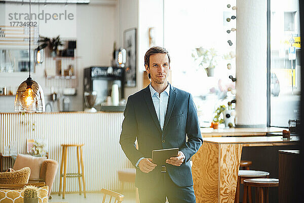 Selbstbewusster Geschäftsmann mit Tablet-PC steht im Café