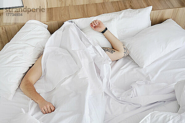 Junger Mann schläft zu Hause unter einer Decke im Bett