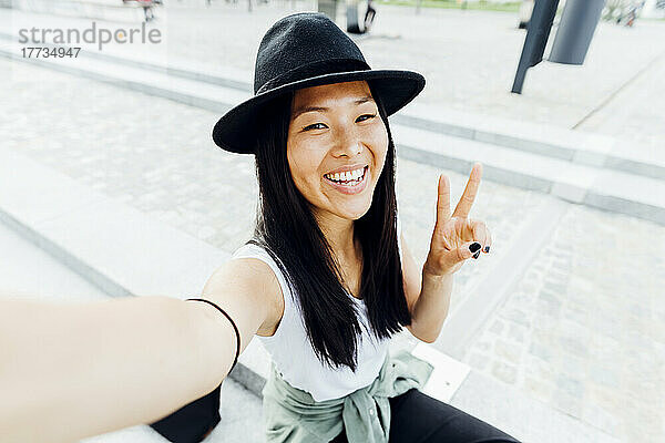 Happy woman wearing hat gesturing peace sign