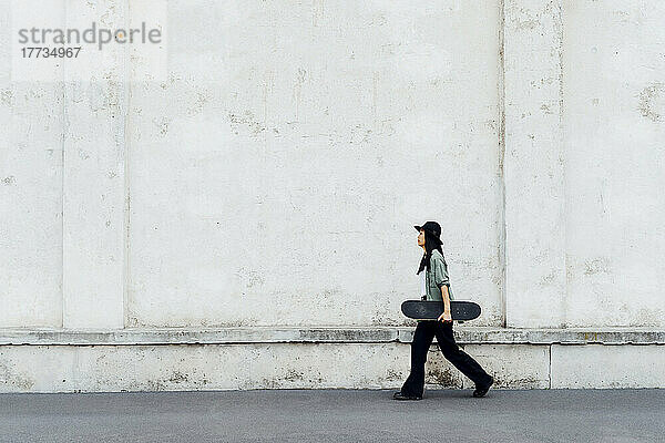 Young woman with skateboard walking by wall