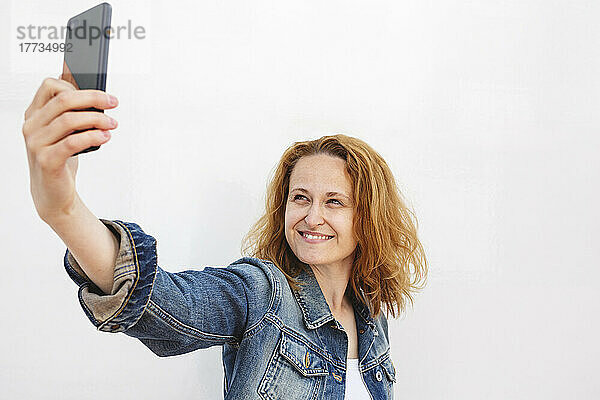 Lächelnde Frau  die vor weißem Hintergrund ein Selfie per Smartphone macht
