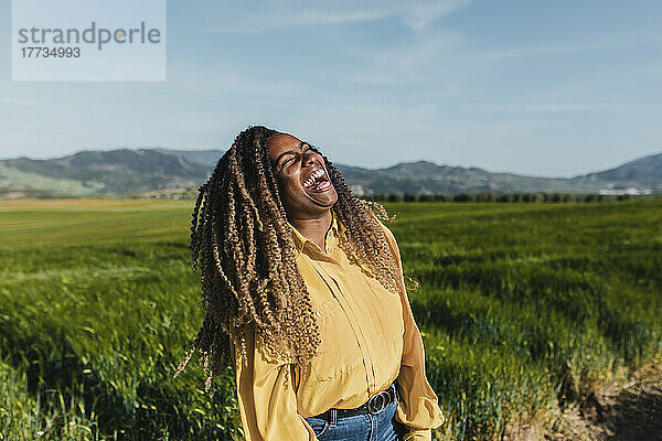Junge Frau mit lockigem Haar lacht an einem sonnigen Tag auf der Wiese
