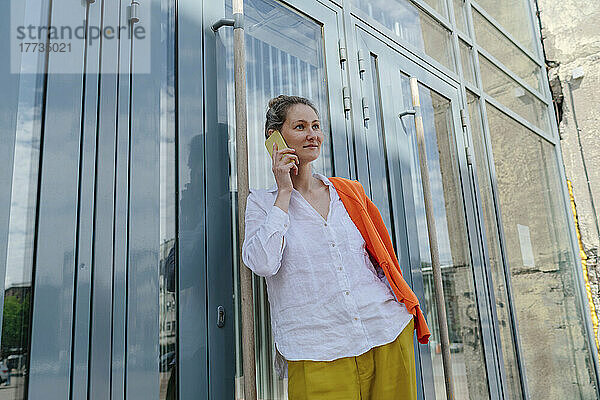 Frau spricht mit Smartphone und lehnt an Glastür