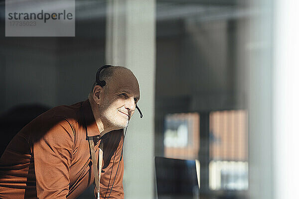 Lächelnder Geschäftsmann mit Headset im Büro  gesehen durch das Fenster