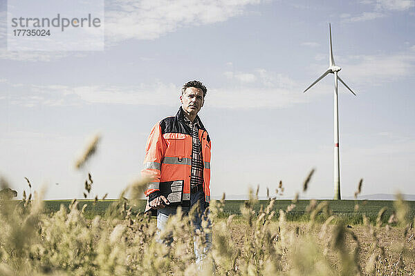 Ingenieur geht an einem sonnigen Tag auf dem Feld in der Nähe der Windkraftanlage spazieren